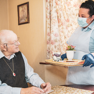 nurse and support worker in blue providing home help service to elderly gentlemen with glasses