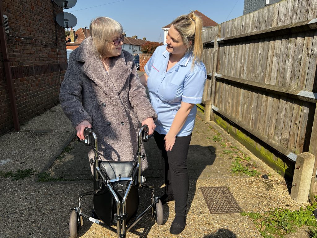 lady in grey coat getting support and help from one of the Comfort Care at Home nurses while walking outside 