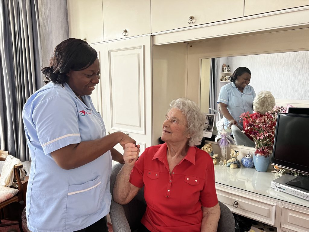 nurse holding elderly ladies hand in her room