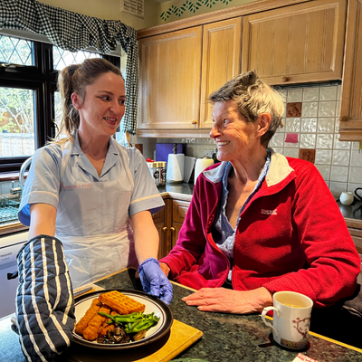 lady in red fleece getting help in the kitchen making food by a professional carer.