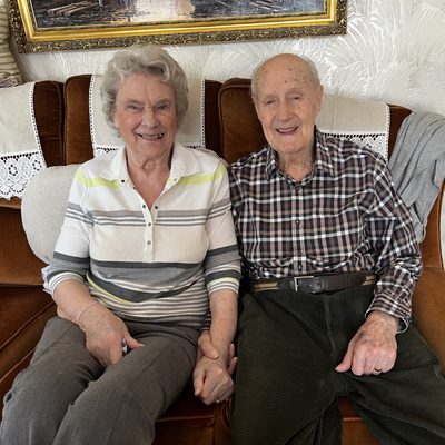 elderly couple smiling sitting on the sofa together holding hands.