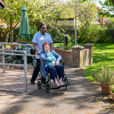 nurse helping lady with brown hair in the wheel chair around a park