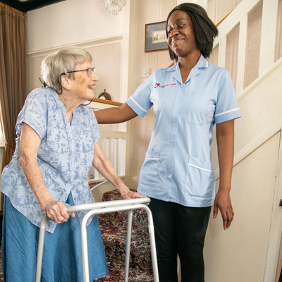 Female care professional assisting a female client who had a stroke with walking to her living room
